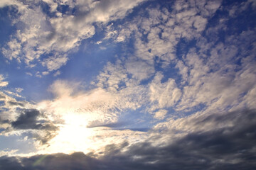 Naklejka na ściany i meble The bright sun hid behind light white clouds in the blue sky.