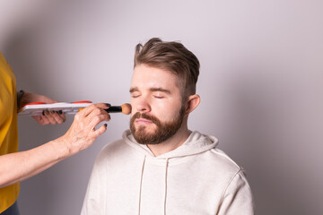 Bearded man getting makeup. Hand of visagist using brush.
