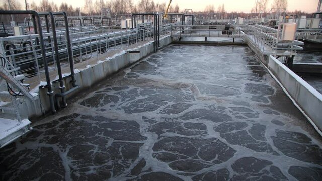 Dirty foamy water swirls at aeration in huge reservoir at contemporary purification station at sunset light in winter evening