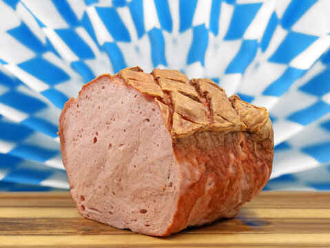 warm bavarian meat loaf or leberkaese on a wooden plate served in front of a typical bavarian diamand pattern