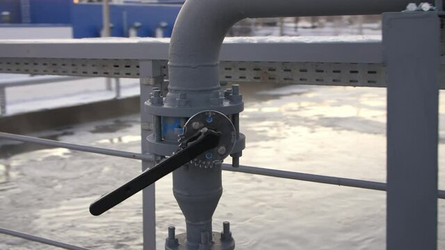 Black levers on pipes near reservoir with swirling water at contemporary purification station at sunset in winter closeup