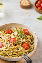 Spaghetti pasta with pesto sauce and cherry tomatoes in a plate close-up.