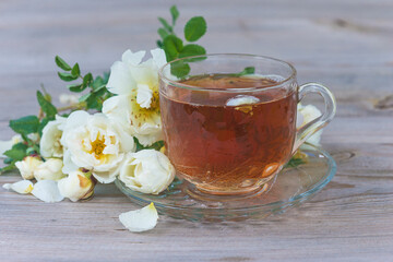 Glass cup of tea and white wild rose flowers on wooden background close up