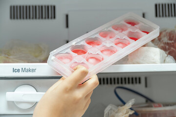 The girl takes out ice molds from the freezer to cool water and drinks.