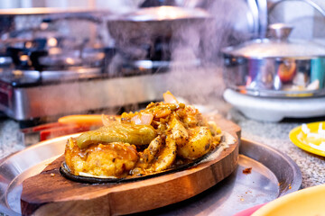 Indian asian sizzler dish served on a wooden tray with an iron hot plate that causes the vegetables like cabbage potato rice to cook and give off smoke as the dish is served to people