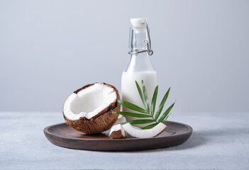 Healthy milk bottle with half coconuts and palm branch in wooden plate on blue background. Front...