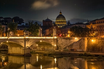 The Basilica of St. Peter in the Vatican is visible from the Eliev Bridge and the Tiber River. Night photo against the background of the starry sky. Rome, Italy