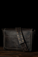 Back view of a retro style dark leather messenger bag isolated on black background.