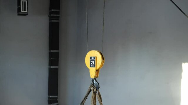 Large heavy cargo hangs on yellow hook in brightly lit spacious workshop premise at contemporary production plant