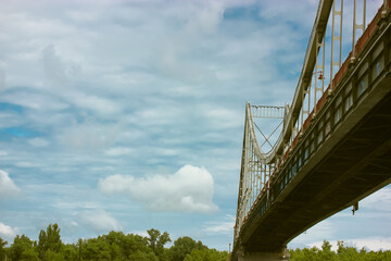 A modern pedestrian cable-stayed bridge against a blue cloudy sky in summer day.