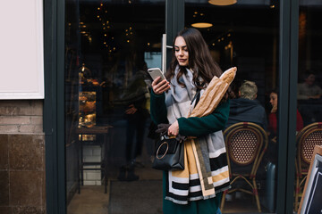 Pleased woman using smartphone while going out of bakery