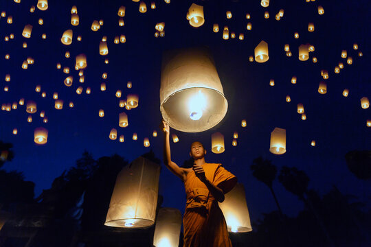 Buddhist Monk releasing lanterns into sky at night, Thailand