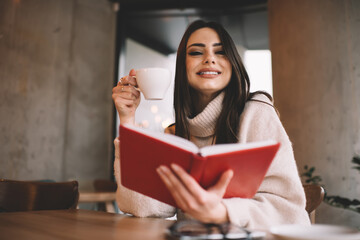 Cheerful woman having coffee and reading book