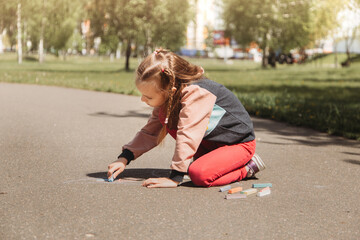 Girl preschooler draws with chalk on the asphalt in summer in the park