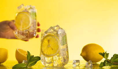 Lemonade with fresh slice lemon and mint leaves. Woman holding glass of lemonade. Summer homemade...