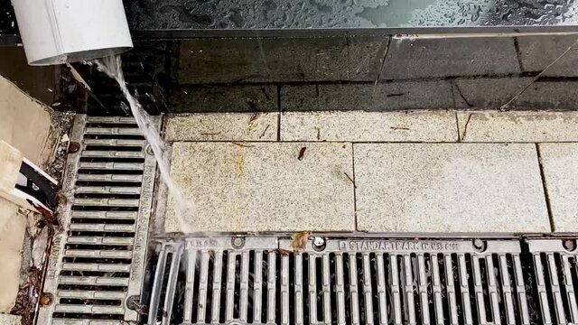 A new shiny storm drainage during the rain. The water pours out of the drainpipe and goes through the grate to the ground
