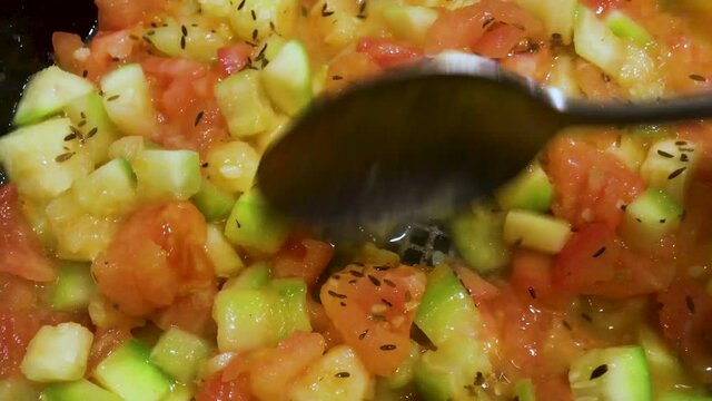 Simmering stewed vegetables - tomatoes and zucchini, sprinkled with dry cumin, stir with a spoon