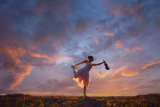 Woman standing outdoors on one leg holding a violin at sunset, Thailand