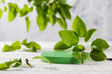 Green round podium surrounded by young leaves, for product presentation on a wooden background. The organic concept.