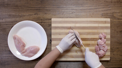Woman hands with a knife slice a chicken fillet on a wooden cutting board