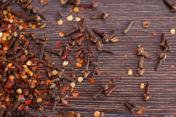 Dry cloves spice and red hot chili pepper flakes on a wooden background. Healthy, spicy ingredient for cooking