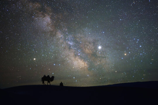 Silhouette of a man and his camel in desert under milky way, Mongolia