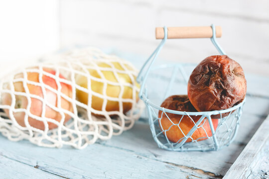 Two rotten apples on a table next to fresh ripe apples