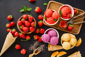 Heap of strawberry and orange, dried lavender with cups of ice cream and cones. Lavender, strawberry and orange sorbet on black background. - obrazy, fototapety, plakaty