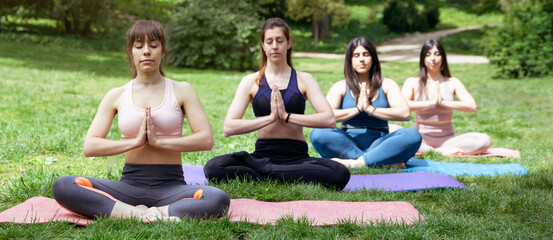 Four women doing meditation outdoors. Group yoga exercises in the park.