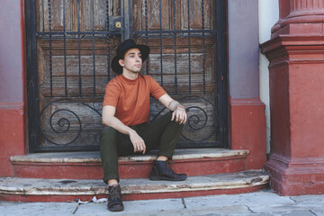 Handsome young man wearing hat. Street portrait of sitting young person.