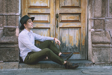 Handsome young man wearing hat. Street portrait of sitting young person.