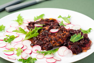 Vegetable diet food. Beetroot steak, radish and frieze salad leaves on a plate on a green background. Close-up