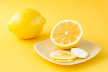 Sliced lemon on a saucer and a whole lemon next to it on a yellow background. Detox fruit diet, body detoxification