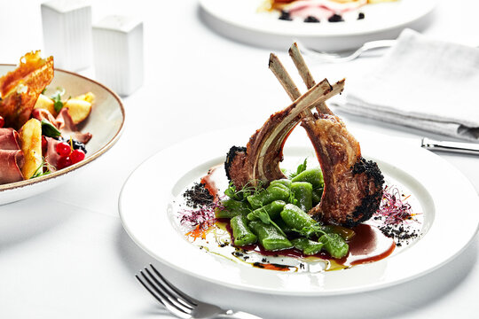 Grilled rack of lamb on a white plate with stewed bean pods. Restaurant serving rack of lamb from the chef.