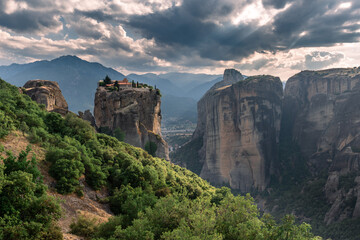 Fototapeta na wymiar Scenic landscape of a wide mountain valley in Greece with bizarre cliffs, a dense forest at the foot of the mountains, and a small Christian monastery on top of a cliff