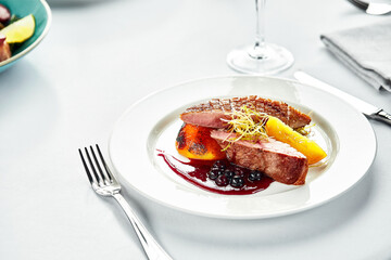 Grilled duck breast with peaches in berry sauce, grilled duck fillet on a white plate, banquet serving of duck meat on a wedding table