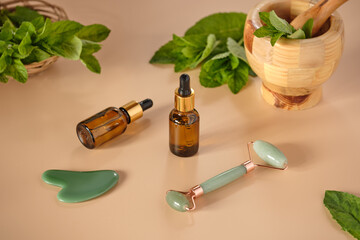 Mint essential oil bottle on a beige background with mint leaves and natural jade guasha face massager. Natural skin care cosmetics.