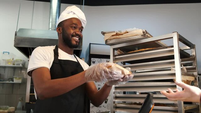 African American baker in uniform sorting baked products on pallets