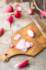 Fresh chopped radishes and a knife on a cutting board on a wooden table. Vegetables for a vegetarian diet. Rustic style. Vertical view