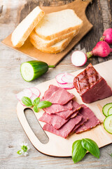 Fresh sliced marbled beef pastrami and vegetables on a cutting board. American delicacy. Rustic style. Vertical view