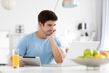 Indoor shot of a smiling European young man surfing the internet on a laptop, messaging on via...