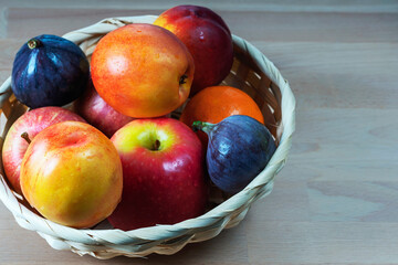 ripe delicious apricots, apples and figs in a wicker basket on a wooden background