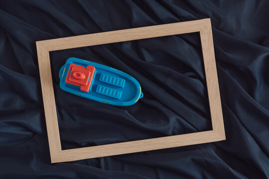Toy boat in a picture frame arranged on dark blue fabric.Minimal aesthetic summer sea concept.