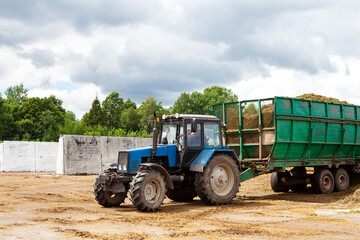 Obraz premium A tractor with a large trailer, unloads the silage into a trash.