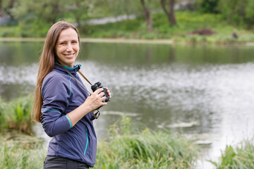 Young woman standing with binoculars near the pond