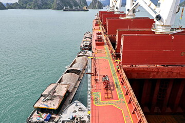 Loading bulk cargo of limestone from barges into a bulk carrier by using ship cranes and grabs at...