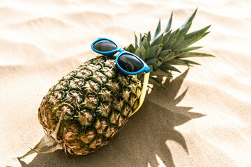 Piña con gafas de sol graciosa en la arena de la playa junto a palmeras y el mar de fondo