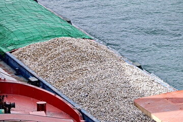 Loading bulk cargo of limestone from barges into a bulk carrier by using ship cranes and grabs at...