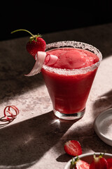 Frozen strawberry rhubarb cocktail with a pink salt rim in hard light.