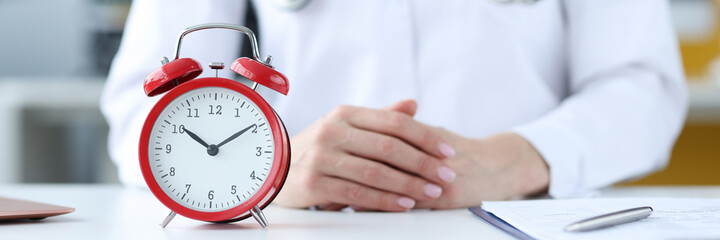 Doctor therapist sitting in office in front of red alarm clock closeup